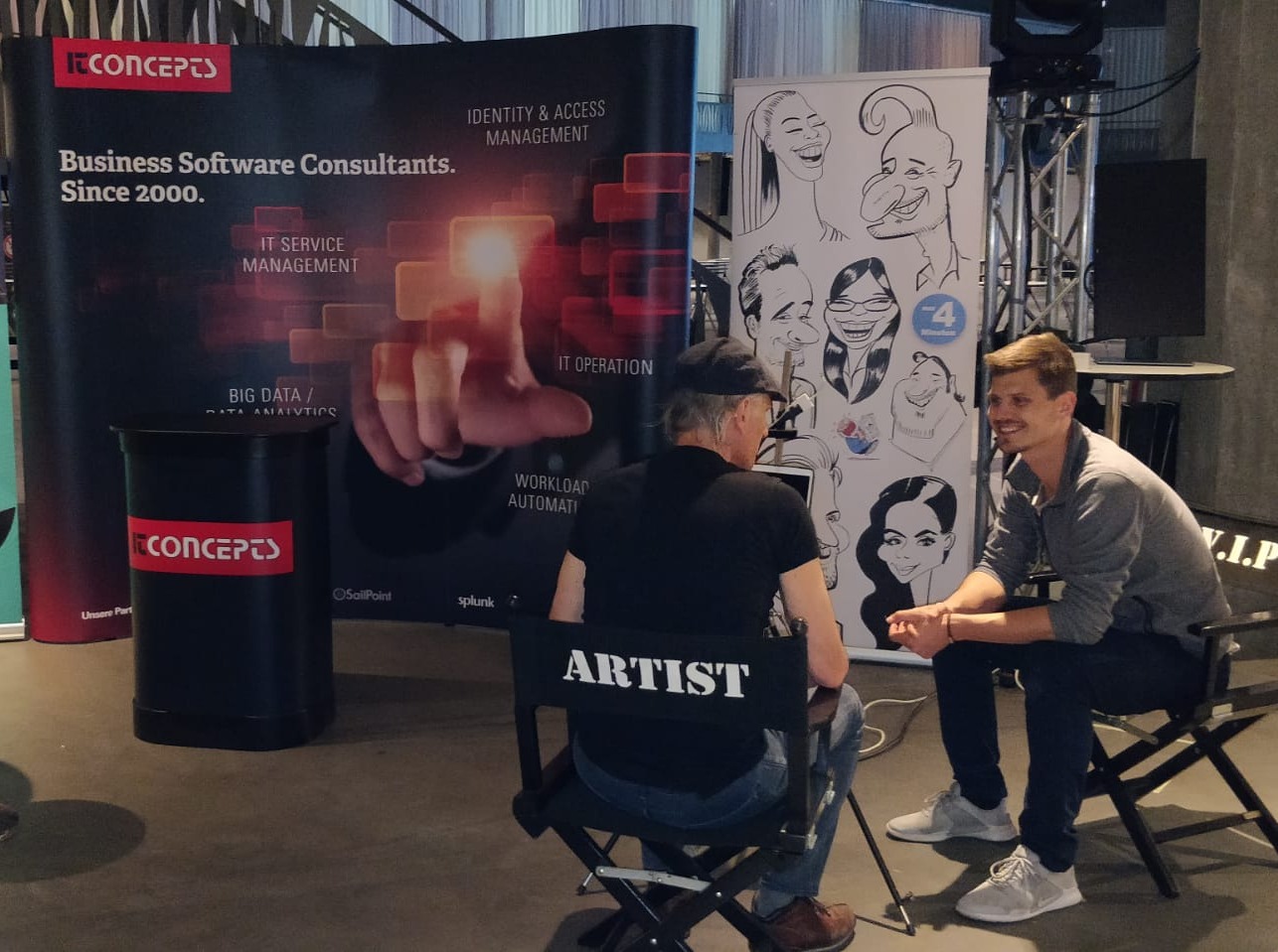 Stand IT Concepts : l'artiste dessine en direct, l'invité assis face à lui sur le siège VIP